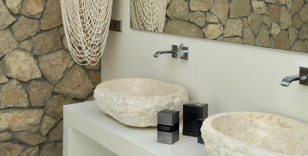 projeto com banheiro clean e sofisticado, cuba de mármore travertino é a protagonista do ambiente, harmonizando perfeitamente com a parede revestida por pedra natural