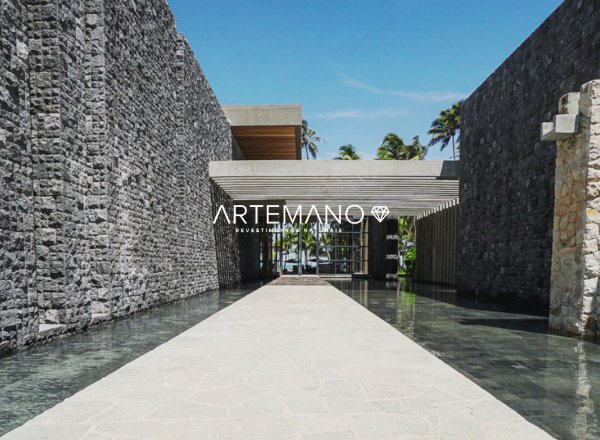 Área externa com espelho d'água revestido por pedra Hitam Artemano e, nas laterais, há duas grandes paredes revestidas por pedras naturais.