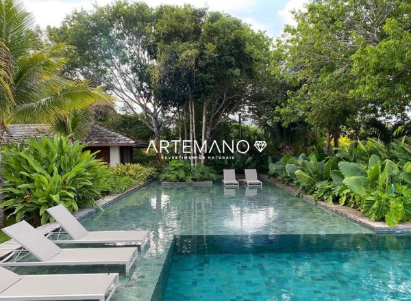 Área externa projeta com belo projeto paisagístico harmonizando com a pedra hijau e espelho d’água em meio à piscina.